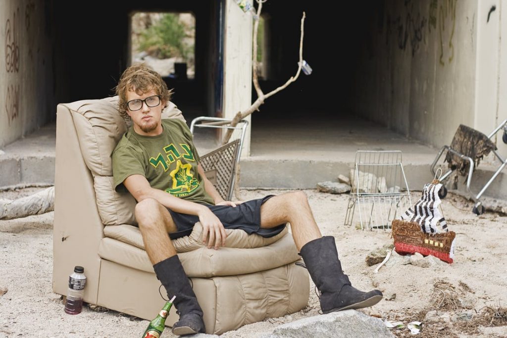 young man with glasses on leather sofa chair outside in dirt