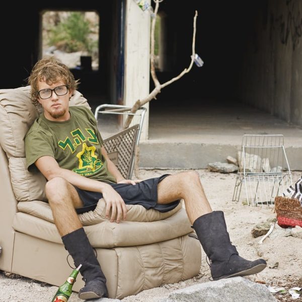 young man with glasses on leather sofa chair outside in dirt
