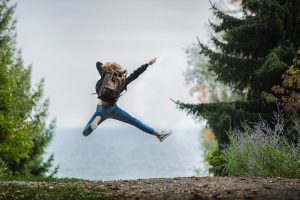 woman with backpack jumping in the air near body of water