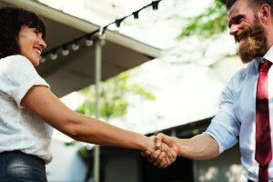 woman in white shaking hands with bearded man in dress shirt and tie