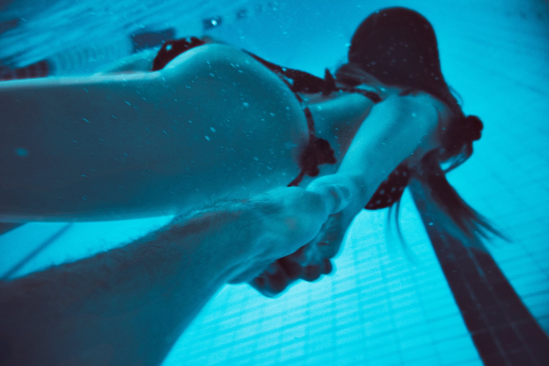 woman holding man's hand underwater in a pool