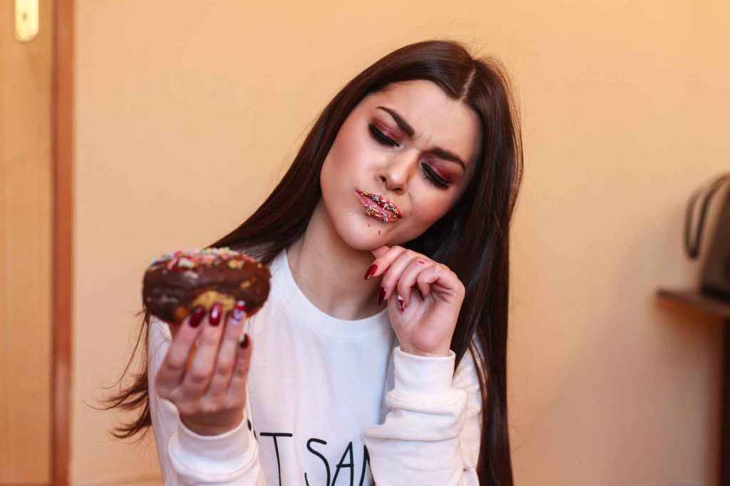 girl with sprinkles on her lips looking inquisitively at donut