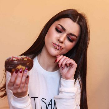 girl with sprinkles on her lips looking inquisitively at donut